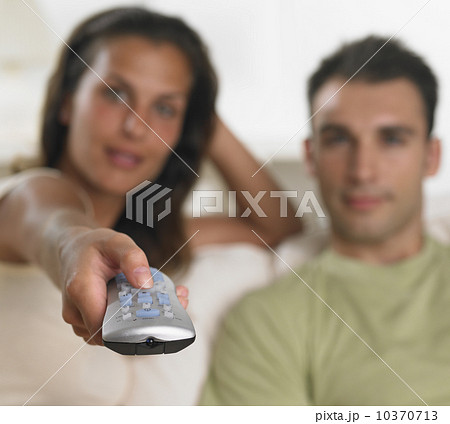 Couple sitting on sofa pointing remote control 10370713