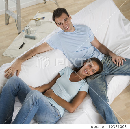 Couple on sofa with paint cans and paintbrushes on floor 10371003