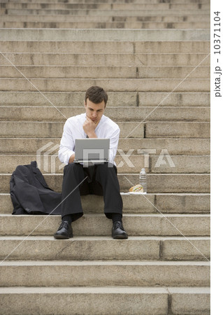 Man sitting outdoors on stairs with laptop Man sitting outdoors on stairs with laptop 10371104