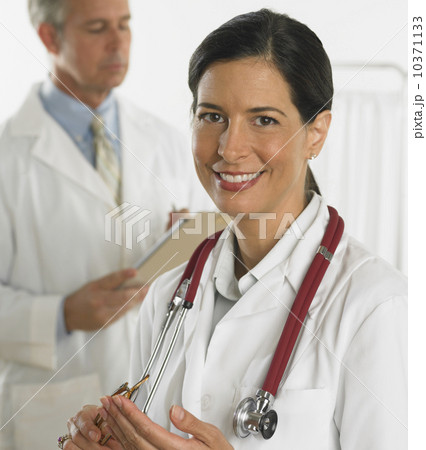 Female doctor smiling with doctor in background Female doctor smiling with doctor in background 10371133