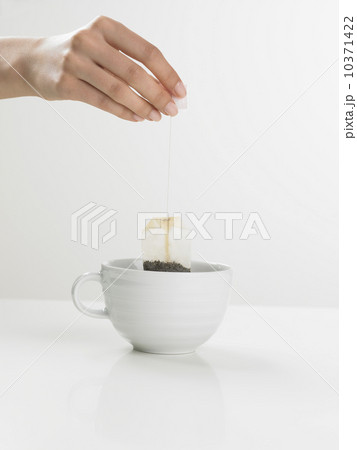 Studio shot of tea cup with woman's hand holding tea bag Studio shot of tea cup with woman's hand holding tea bag 10371422