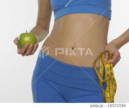 Woman in athletic gear holding apple and tape measure 10371594