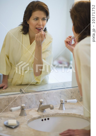 Woman putting on lipstick in bathroom Woman putting on lipstick in bathroom 10371752