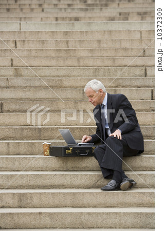 Man sitting outdoors on stairs with laptop 10372309