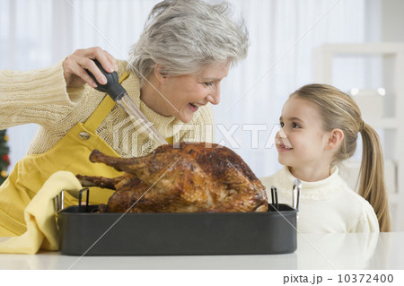 Grandmother and daughter basting roast turkey 10372400