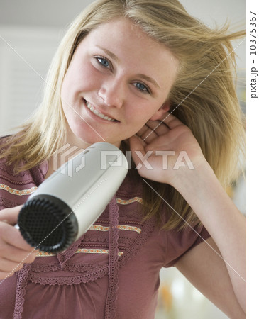 Teenaged girl blow drying hair Teenaged girl blow drying hair 10375367