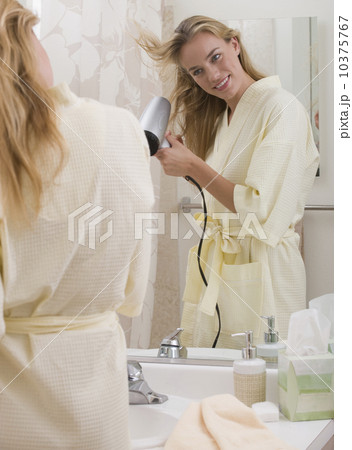 Woman blow-drying hair in bathroom Woman blow-drying hair in bathroom 10375767