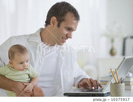 Father working on laptop and holding son Father working on laptop and holding son 10375917