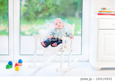 Funny newborn baby boy in a white rocking chair next to a big wi 10414942