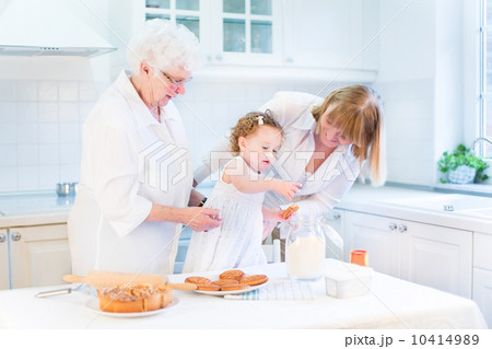 Cute curly toddler girl baking a pie with her grandmothers in a 10414989