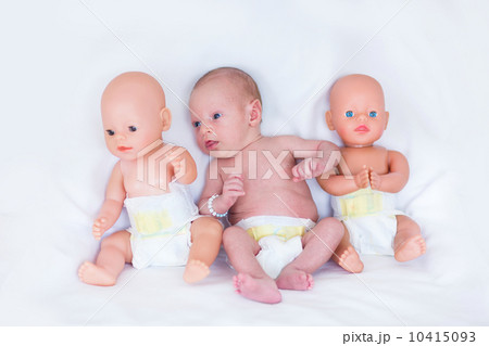 Funny newborn baby in a diaper between two plastic dolls on whit 10415093