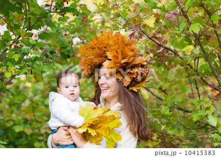 Young beautiful woman in a maple leaf wreath holding a baby in a park 10415383