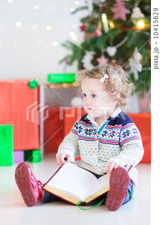 Cute toddler girl with curly hair reading a book under a beautif Cute toddler girl with curly hair reading a book under a beautif 10415629