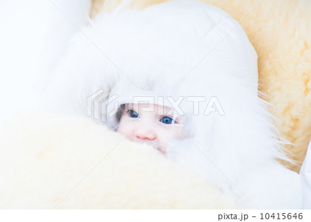 Baby girl in a white fur jacket sitting in a stroller with a warm sheepskin foot muff 10415646