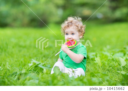 Beautiful curly baby girl eating watermelon candy in a summer pa Beautiful curly baby girl eating watermelon candy in a summer pa 10415662