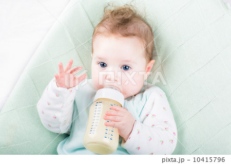 Adorable baby girl on a green knitted blanket drinking milk Adorable baby girl on a green knitted blanket drinking milk 10415796