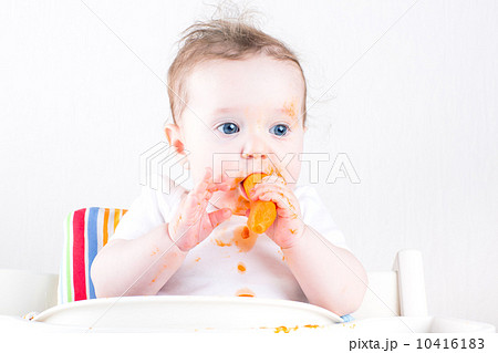 Sweet little baby eating a carrot in a white high chair Sweet little baby eating a carrot in a white high chair 10416183