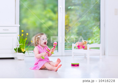 Cute curly toddler girl playing tambourine in a sunny white room 10416228