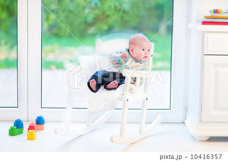 Funny newborn baby boy relaxing in a white rocking chair at a bi Funny newborn baby boy relaxing in a white rocking chair at a bi 10416357
