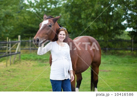 Attractive young pregnant woman and a horse standing in a field Attractive young pregnant woman and a horse standing in a field 10416586