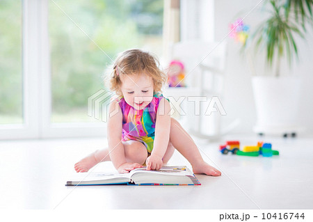 Funny toddler girl reading a book sitting on a fllor in a white Funny toddler girl reading a book sitting on a fllor in a white 10416744