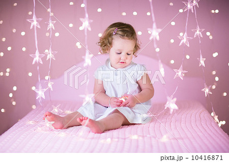 Cute toddler girl with curly hair in a white dress playing in a 10416871