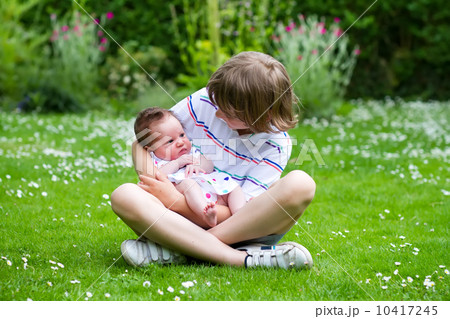 Cute boy sitting in a beautiful summer garden full with flowers holding his newborn sister 10417245