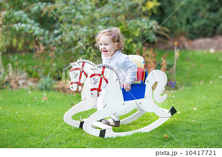 Cute happy litlte girl on a rocking horse in the garden Cute happy litlte girl on a rocking horse in the garden 10417721