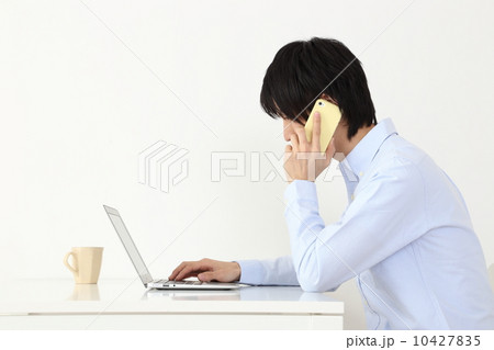 インターネットをしながら電話をする男性 10427835
