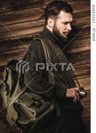 Handsome man wearing cardigan with backpack and vintage camera in house interior Handsome man wearing cardigan with backpack and vintage camera in house interior 10428809