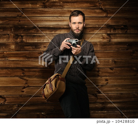Handsome man wearing cardigan with vintage camera in wooden house interior Handsome man wearing cardigan with vintage camera in wooden house interior 10428810