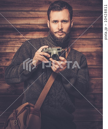 Handsome man wearing cardigan with vintage camera in wooden house interior 10428811