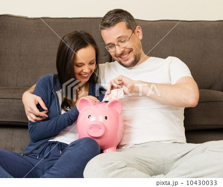 Cheerful young couple putting banknote in piggybank 10430033