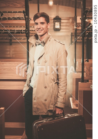 Handsome young man with suitcase in coat inside vintage train coach 10430895