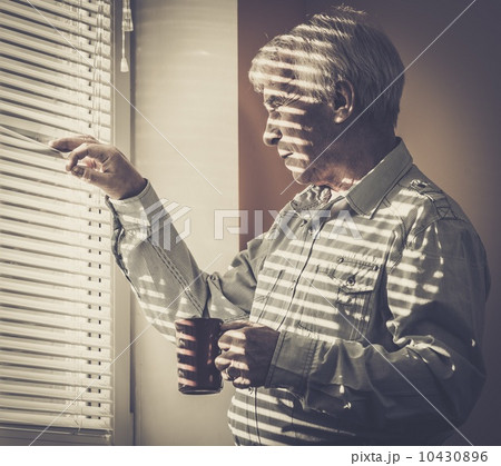 Senior man with cup looking out the window through jalousie 10430896
