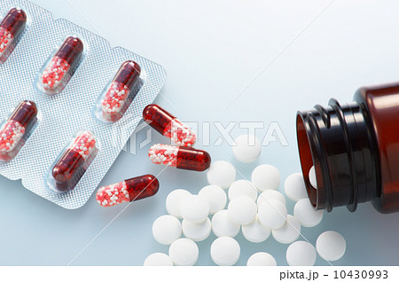 赤いカプセル薬とボトルからこぼれた錠剤の写真素材