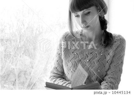 Young adult girl reading book near the window. Black and White image Young adult girl reading book near the window. Black and White image 10445134