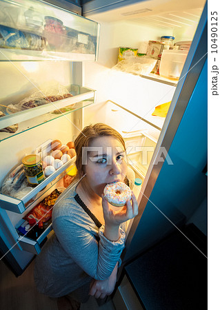 woman in pajamas eating donut next to refrigerator woman in pajamas eating donut next to refrigerator 10490125
