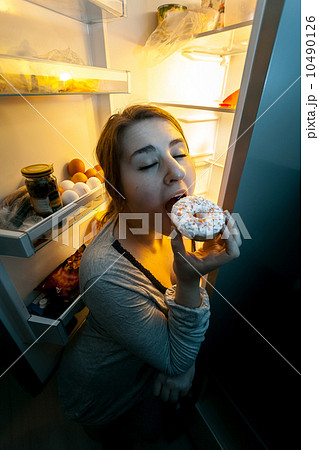 woman in pajamas eating donut on kitchen at night woman in pajamas eating donut on kitchen at night 10490126