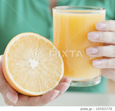 Close up of woman's hands holding half of orange and glass of juice Close up of woman's hands holding half of orange and glass of juice 10503770