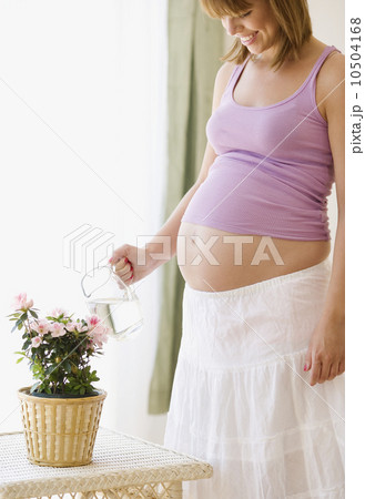 Pregnant woman watering plant 10504168