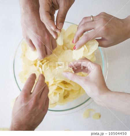 Hands reaching into bowl of chips 10504450