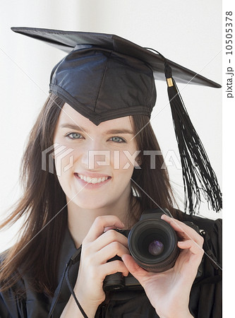 Portrait of young woman in graduation gown holding camera 10505378