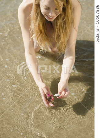 Woman picking up seashells at beach 10507886