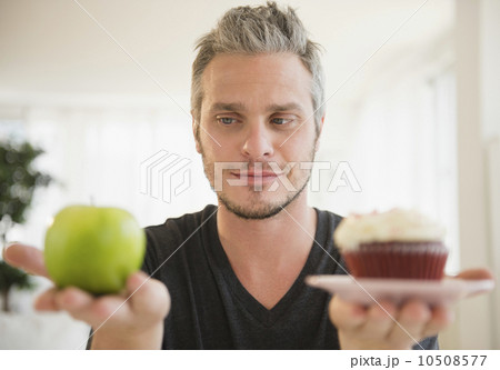 Man weighing green apple against cup cake 10508577