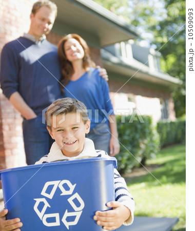 USA, New York, Flanders, Boy (8-9) holding bucket with recycling symbol, parents in background 10509093
