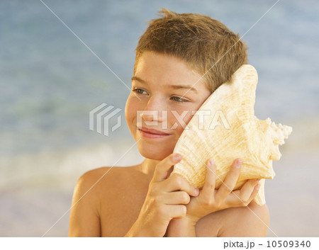 Boy (10-11) listening to sea shell on beach Boy (10-11) listening to sea shell on beach 10509340