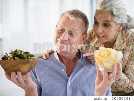Elderly couple choosing between fresh salad and crisps 10509541
