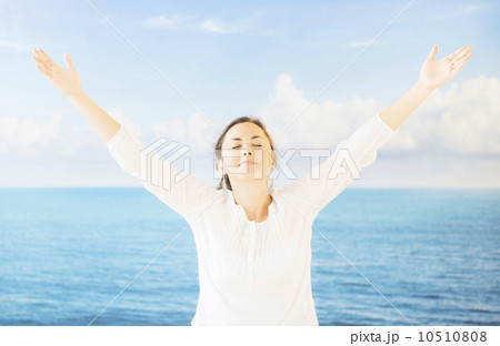 Portrait of woman with arms raised in front of backdrop with sea and sky 10510808