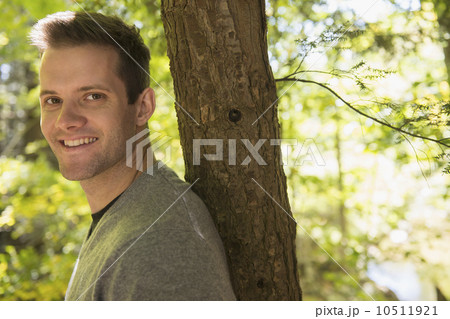 Portrait of young man leaning against tree trunk 10511921